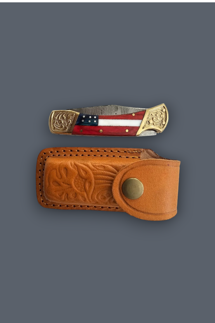 A folding pocket knife with a red, white, and blue flag inlay and ornate brass-toned ends, displayed above its matching tooled brown leather sheath on a dark gray background.