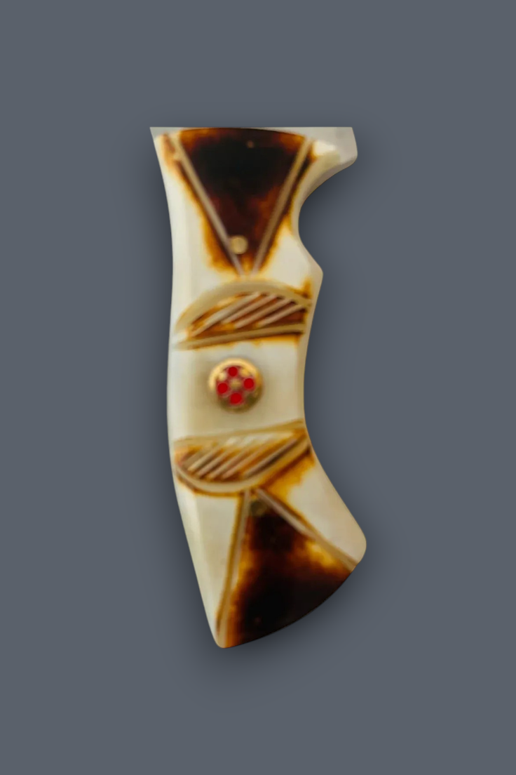 A decorative handle scale or grip cover with a cream-colored background, dark brown geometric patterns, and a small red and gold center emblem, shown against a solid dark gray background.