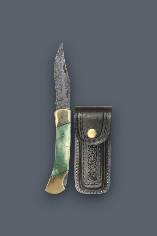 A folding pocket knife with a patterned steel blade, green and gold handle scales, and a black leather sheath, displayed on a solid dark gray background.
