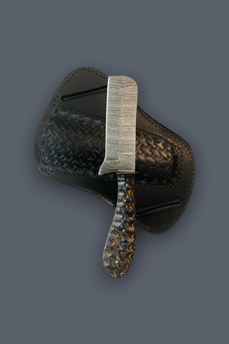 A custom hand-forged knife with a textured silver blade and a patterned handle, resting on a black woven leather sheath against a solid dark gray background.