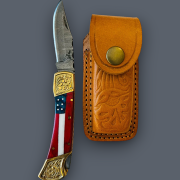 A folding pocket knife with a patterned red, white, and blue handle and gold-toned metal accents, shown next to its tan leather sheath on a solid dark gray background.