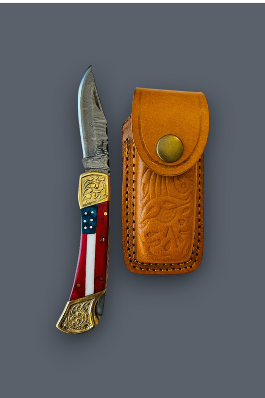 A folding pocket knife with a patterned red, white, and blue handle and gold-toned metal accents, shown next to its tan leather sheath on a solid dark gray background.