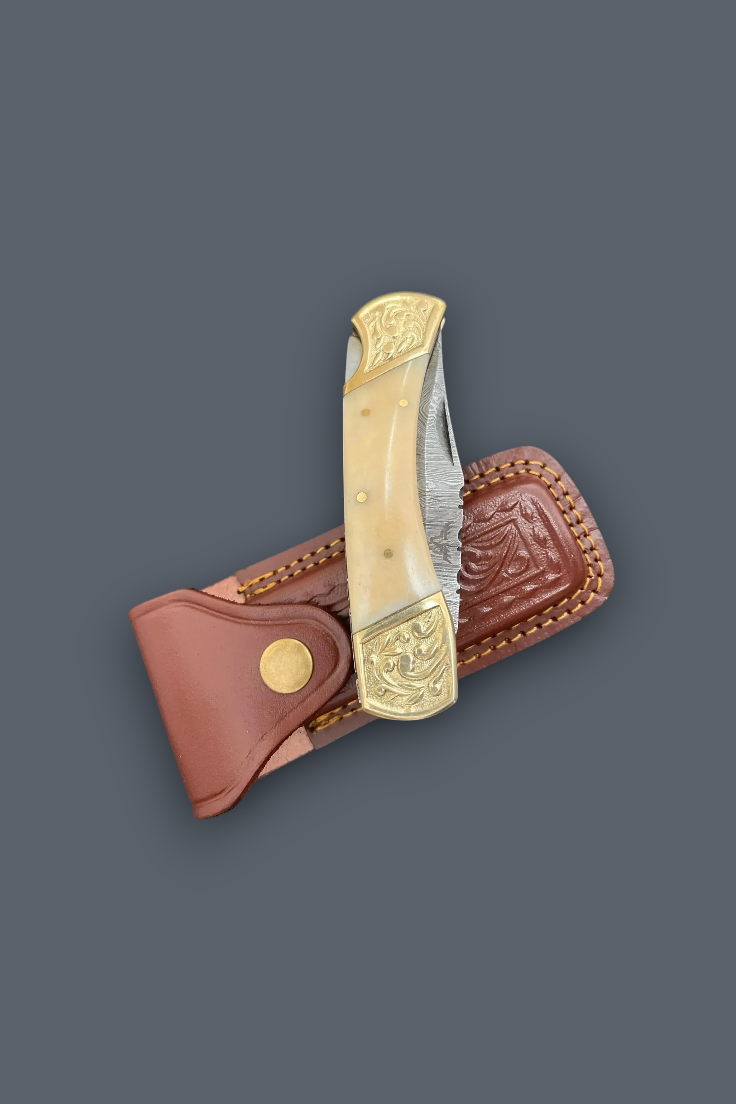 A folding pocket knife with a cream bone handle and gold-toned metal fittings, shown partially inserted into a brown leather sheath on a dark gray background.