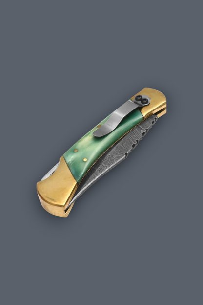 A folding pocket knife with a green inlay handle, gold-toned metal end caps, and a partially serrated gray patterned blade, shown on a solid dark gray background.
