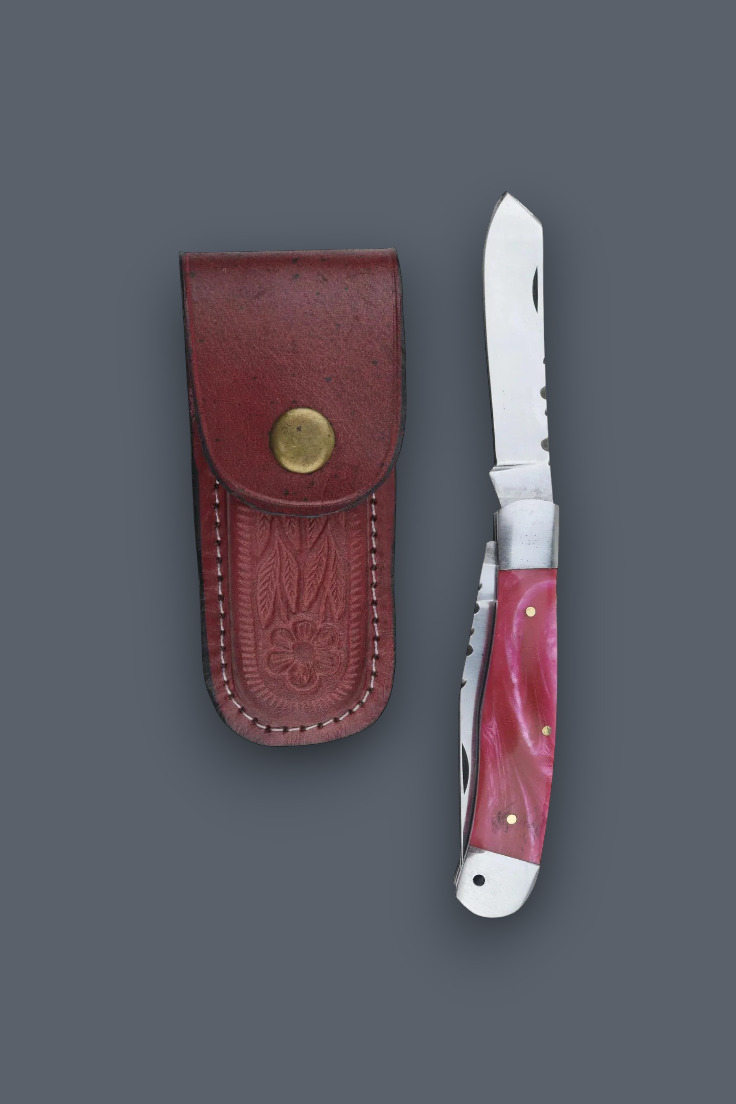 A folding pocket knife with a pink marbled handle and silver blade, shown next to its reddish-brown leather sheath with a brass snap button, on a dark gray background.
