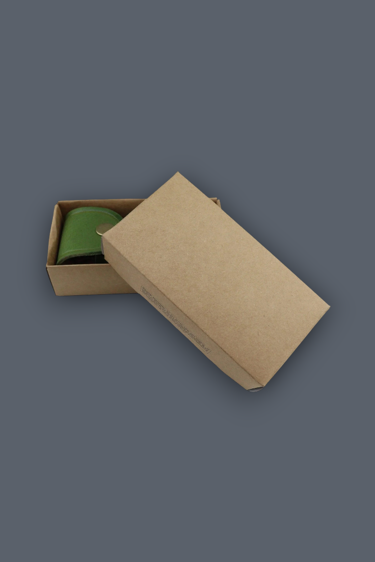 A brown kraft paper gift box with its lid partially open, revealing a green cylindrical item inside, set against a solid dark gray background.