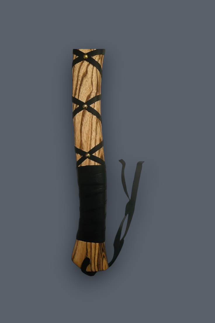 A wooden staff or rod with a natural wood grain finish, wrapped in black leather at the base and accented with black leather criss-cross bands, shown on a solid dark gray background.