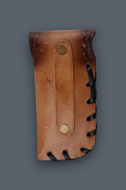 A brown leather holster or sheath with black stitched edges and brass-tone rivets, shown against a plain dark gray background.