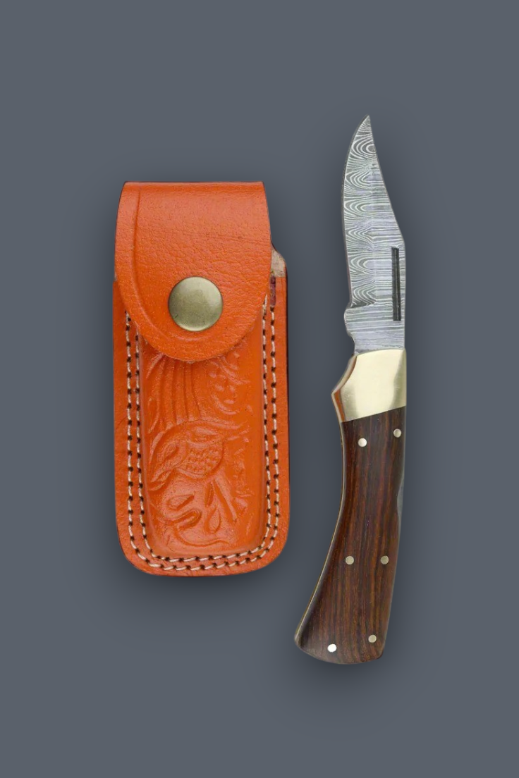 A fixed-blade knife with a patterned steel blade, brass bolster, and dark wood handle, displayed next to its orange leather sheath on a dark gray background.