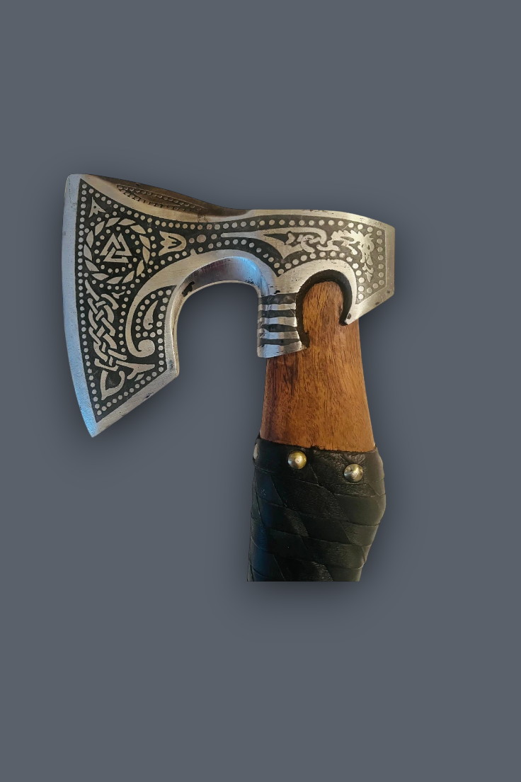 A decorative Viking-style bearded axe with an engraved silver-toned metal head, a brown wooden handle, and a black leather-wrapped grip, shown against a solid dark gray background.