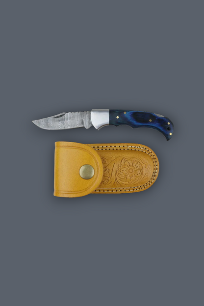 A fixed-blade knife with a textured silver blade and a dark blue handle, displayed horizontally above a tan leather sheath on a solid dark gray background.