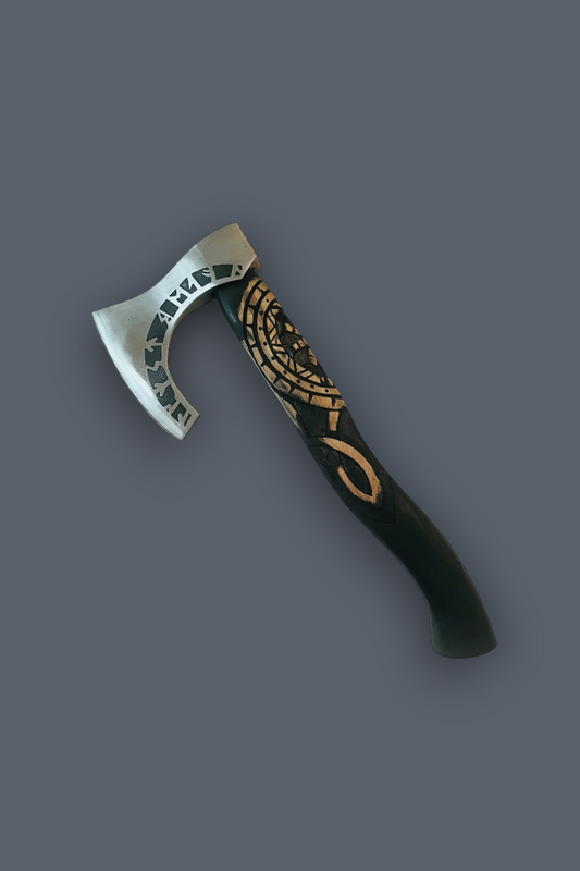 A Viking-style bearded axe with a silver steel blade featuring engraved runes and a black handle decorated with gold Norse knotwork and a runic symbol, shown on a solid dark gray background.