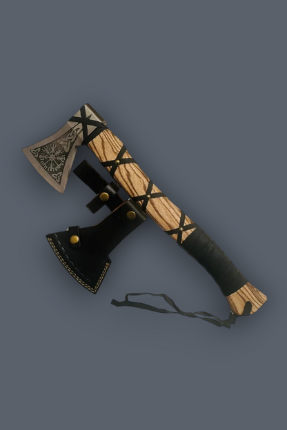 A decorative axe with a carved light wood handle wrapped in black leather, a black leather sheath, and a patterned metal head, shown on a solid dark gray background.