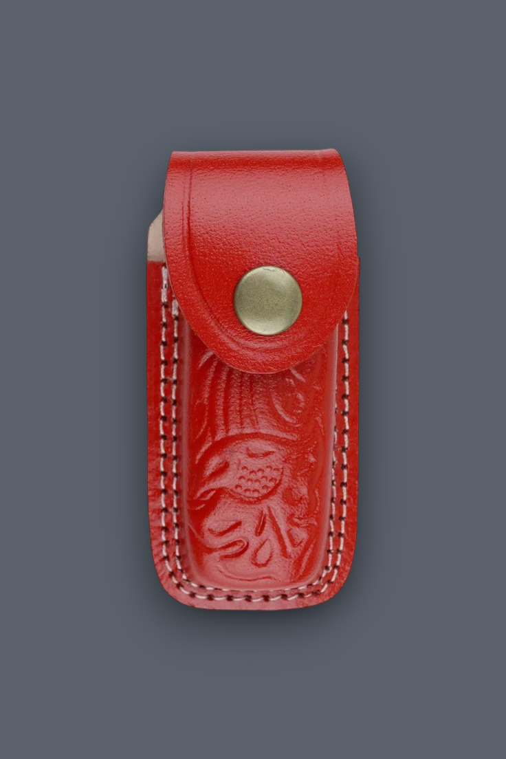 A red leather knife sheath with an embossed floral design and a brass snap button, shown against a solid dark gray background.