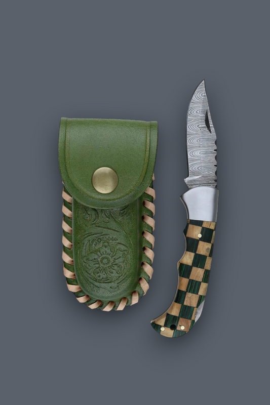 A folding pocket knife with a patterned steel blade and a green-and-tan checkered handle, shown next to its olive green leather sheath on a dark gray background.