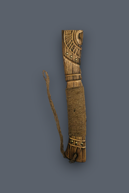 A carved wooden ceremonial or decorative object wrapped with brown cord, featuring geometric engravings and a hanging cord, shown against a solid dark gray background.