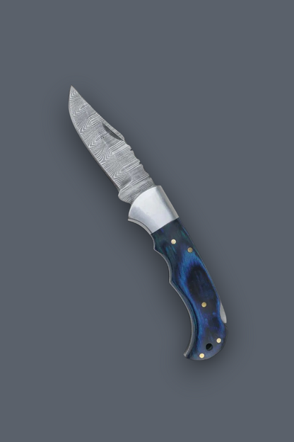 A fixed-blade knife with a patterned steel blade and a contoured handle featuring a blue and black marbled pattern with brass pins, shown on a solid dark gray background.