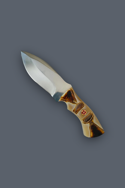A fixed-blade knife with a satin-finished silver blade and a decorative gold-toned handle featuring a small red cross emblem, shown on a solid dark gray background.