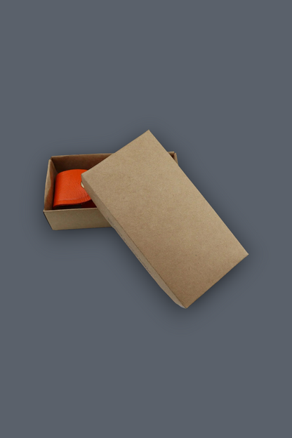 A brown kraft paper gift box with its lid propped open, revealing a bright orange item inside, set against a solid dark gray background.