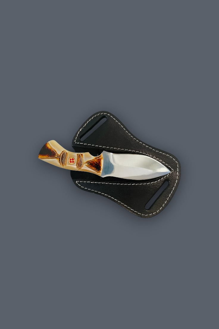 A small fixed-blade knife with a polished silver blade and a gold-toned handle featuring a red cross emblem, resting on a black leather sheath against a solid dark gray background.