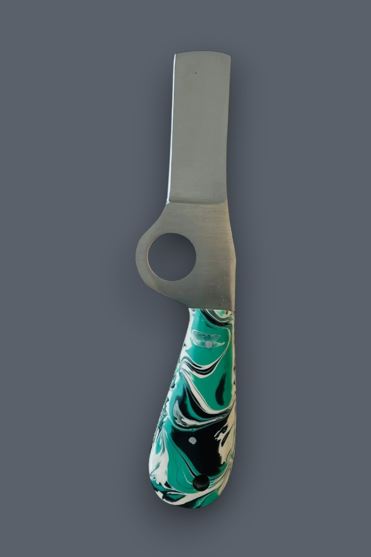 A unique kitchen tool with a flat, rectangular metal blade featuring a circular cutout near the base, and a sculpted handle with a marbled pattern of teal green, black, and white. The tool is displayed vertically against a solid dark gray background.