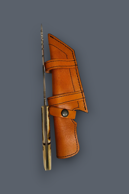 A folding pocket knife with a brass-colored handle and a sharp silver blade, shown partially sheathed in a brown leather sheath against a solid dark gray background.