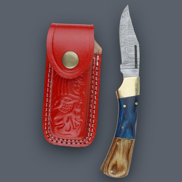 A folding pocket knife with a patterned steel blade, blue and brown handle scales, and a brass snap button, shown next to its red leather sheath on a dark gray background.