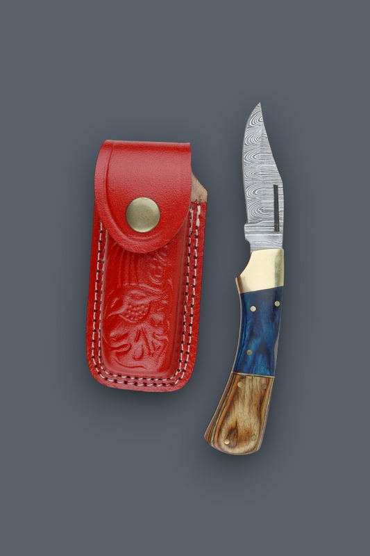 A folding pocket knife with a patterned steel blade, blue and brown handle scales, and a brass snap button, shown next to its red leather sheath on a dark gray background.