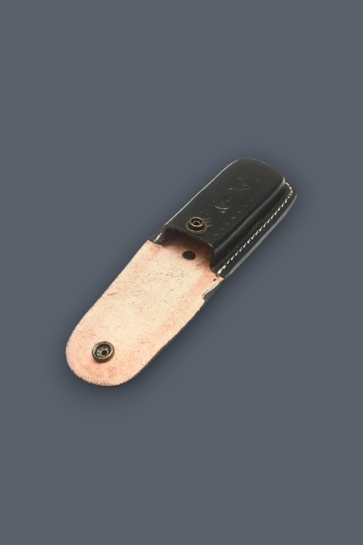 A small leather accessory, likely a pocket clip or card holder, featuring a black leather top section and a warm, copper-toned natural leather bottom section, shown on a solid dark gray background.