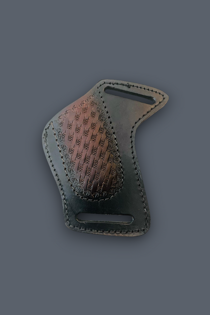 A dark brown leather belt buckle with a textured, embossed chevron pattern on one side and a smooth, polished metallic bronze finish on the other, shown on a solid dark gray background.