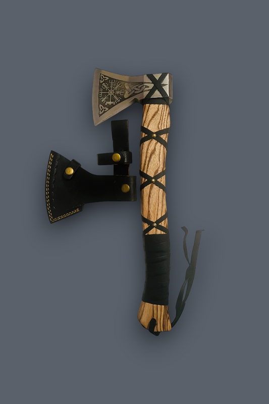 A Viking-style hand axe with a carved wooden handle, black leather wrap, and engraved steel head, shown alongside a black leather sheath on a dark gray background.