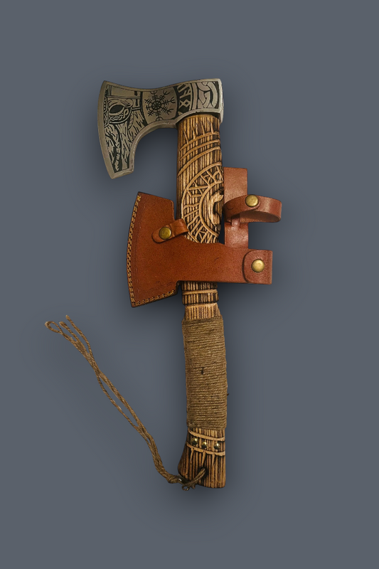 A decorative Viking-style bearded axe with an engraved metal head, a wrapped wooden handle, a brown leather sheath, and a braided cord, displayed against a solid dark gray background.