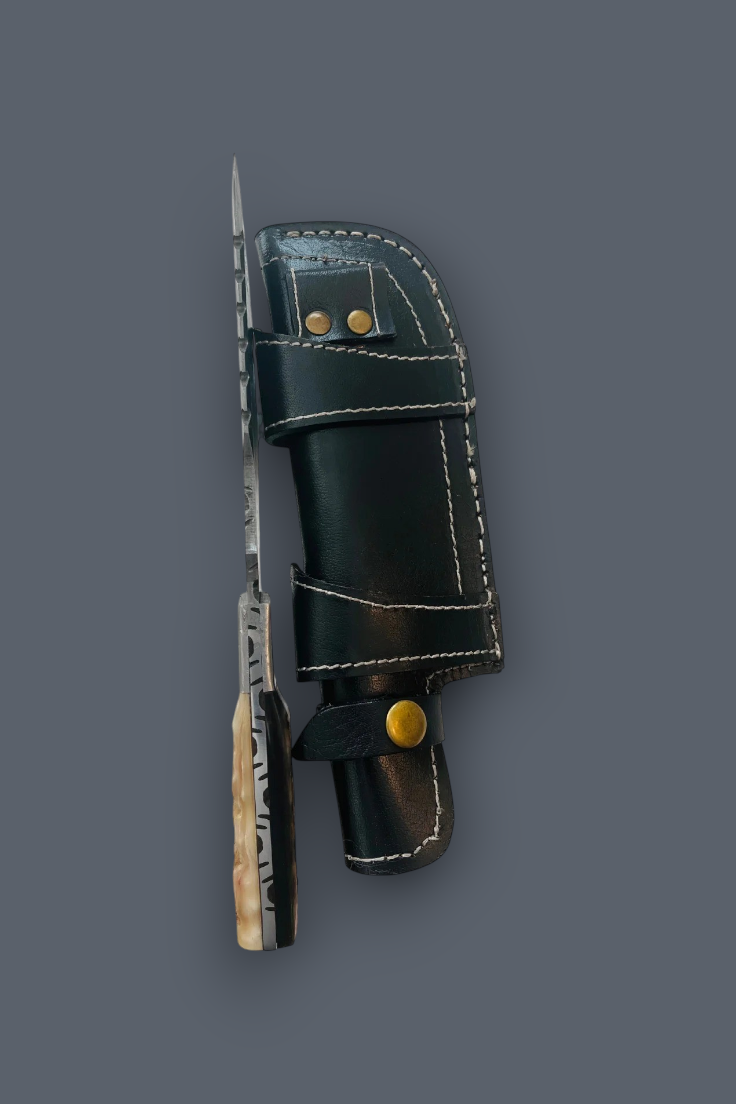 A fixed-blade knife with a patterned silver blade and a textured light handle, shown alongside its black leather sheath with white stitching and brass hardware, set against a solid dark gray background.