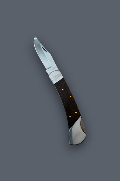 A folding pocket knife with a silver steel blade and a dark brown wooden handle accented by brass pins, shown diagonally on a solid dark gray background.