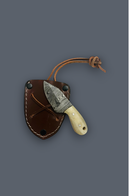 A fixed-blade knife with a patterned steel blade and cream-colored handle, partially tucked into a brown leather sheath with a tan cord, shown on a dark gray background.
