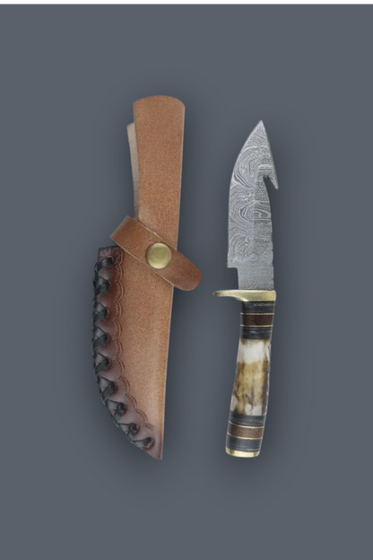 A fixed-blade knife with a patterned steel blade, a horn-like handle, and a brass guard, shown next to its brown leather sheath on a dark gray background.