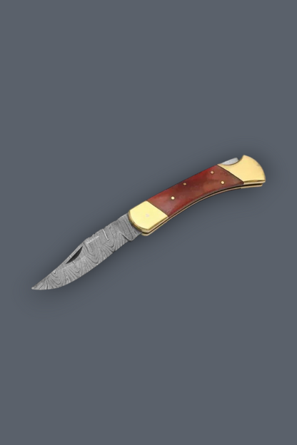 A folding pocket knife with a Damascus steel blade, featuring a reddish-brown wood handle with brass bolsters, shown on a solid dark gray background.