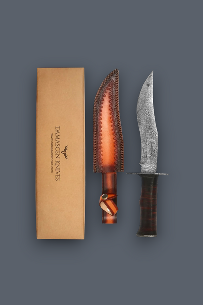 Damascus steel fixed blade knife shown next to its brown leather sheath and tan cardboard box on a dark gray background.