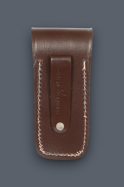 A brown leather knife sheath with white contrast stitching and a central leather tab stamped with the brand 'DALLAS BUCK', shown on a dark slate gray background.