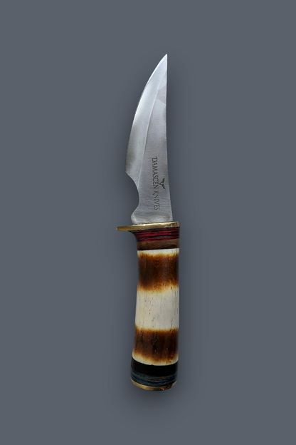 A fixed-blade knife with a curved silver steel blade and a natural horn handle showing brown and cream bands, set against a solid dark gray background.