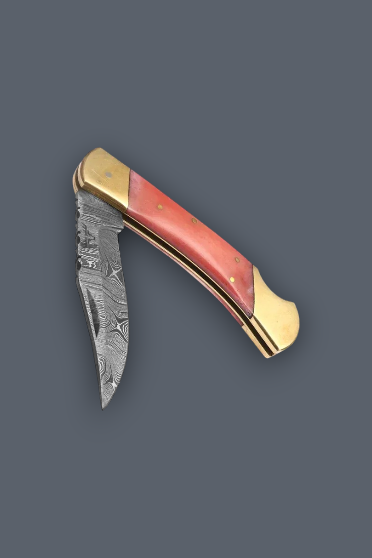 A folding pocket knife with a Damascus steel blade, featuring a coral-pink handle scale and brass bolsters, shown against a solid dark gray background.