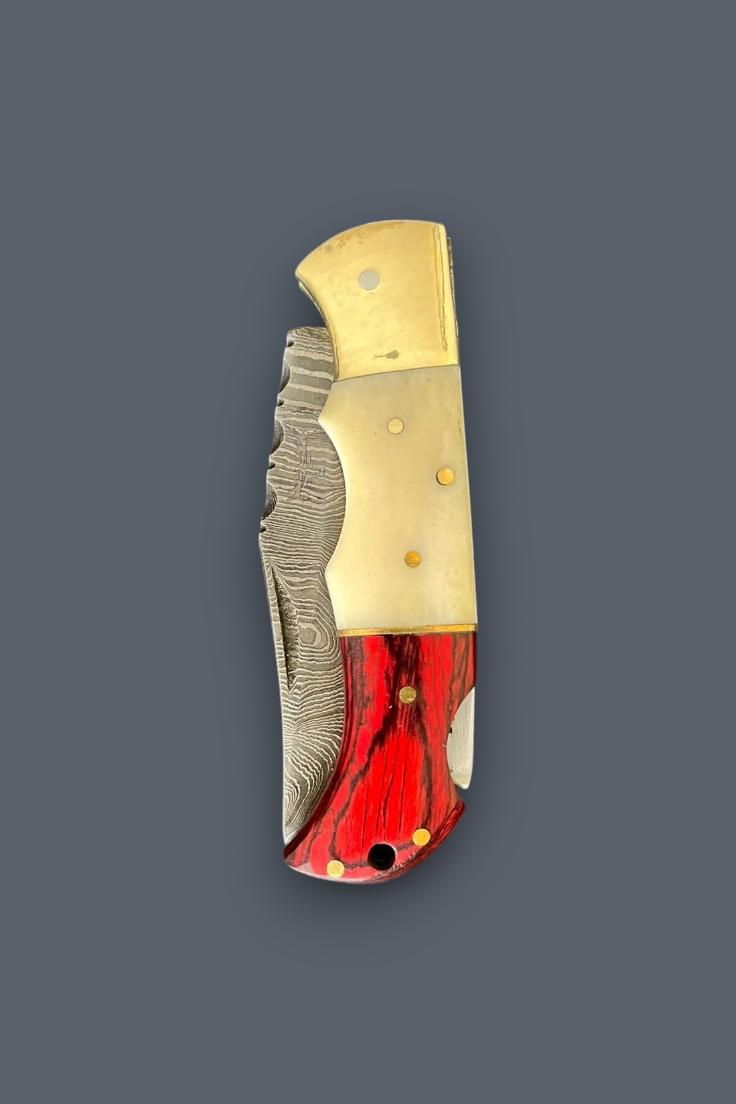 A folding pocket knife with a Damascus steel blade, featuring a gold-toned metal bolster and a red and black marbled resin inlay handle, shown on a solid dark gray background.