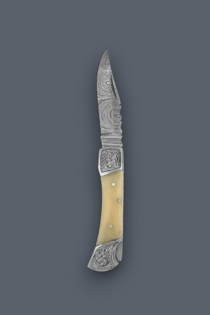 A folding pocket knife with a patterned steel blade, ornate silver-toned metal fittings, and a curved cream-colored bone handle, shown against a solid dark gray background.