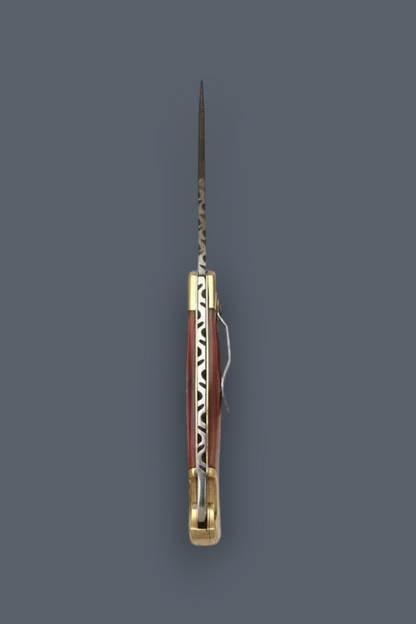 A vintage folding pocket knife with a patterned reddish-brown and white handle, a long steel blade, and brass hardware, shown vertically against a solid dark gray background.