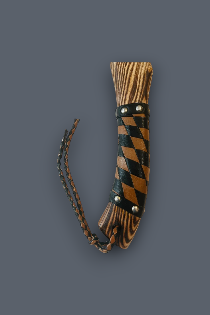 A handcrafted wooden paddle or tool with a dark brown and black striped handle, secured with metal rivets and a braided leather strap, shown against a solid dark gray background.