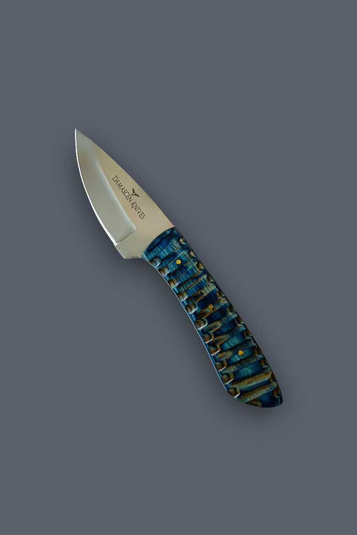 A fixed-blade knife with a satin-finished silver blade and a textured handle featuring a blue, green, and gold pattern, shown on a solid dark gray background.