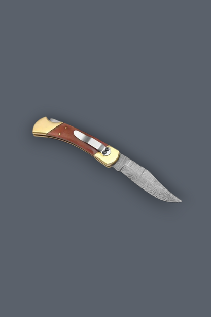 A folding pocket knife with a patterned steel blade, a reddish-brown wooden handle scale, and brass-colored metal accents, shown on a solid dark gray background.