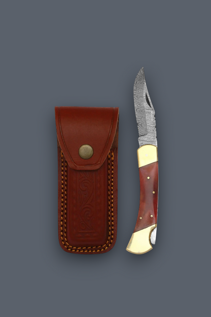 A folding pocket knife with a patterned steel blade, reddish-brown and gold-toned handle, shown next to its brown leather sheath on a dark gray background.