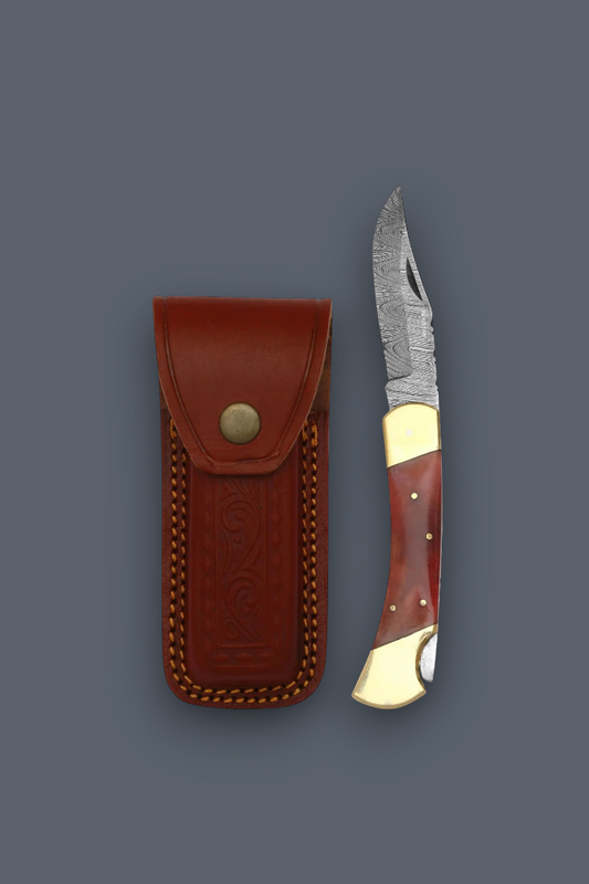 A folding pocket knife with a patterned steel blade, reddish-brown and gold-toned handle, shown next to its brown leather sheath on a dark gray background.