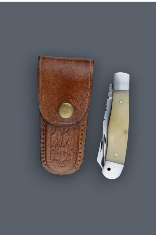 A folding pocket knife with a cream-colored bone handle and silver blade, displayed next to its brown leather sheath with an embossed eagle design and brass snap closure, set against a solid dark gray background.